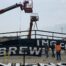 A crane installing a large sign sponsor at a baseball stadium