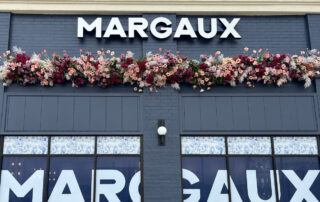 Exterior view of Margaux's building sign with mixed flower decor below it.